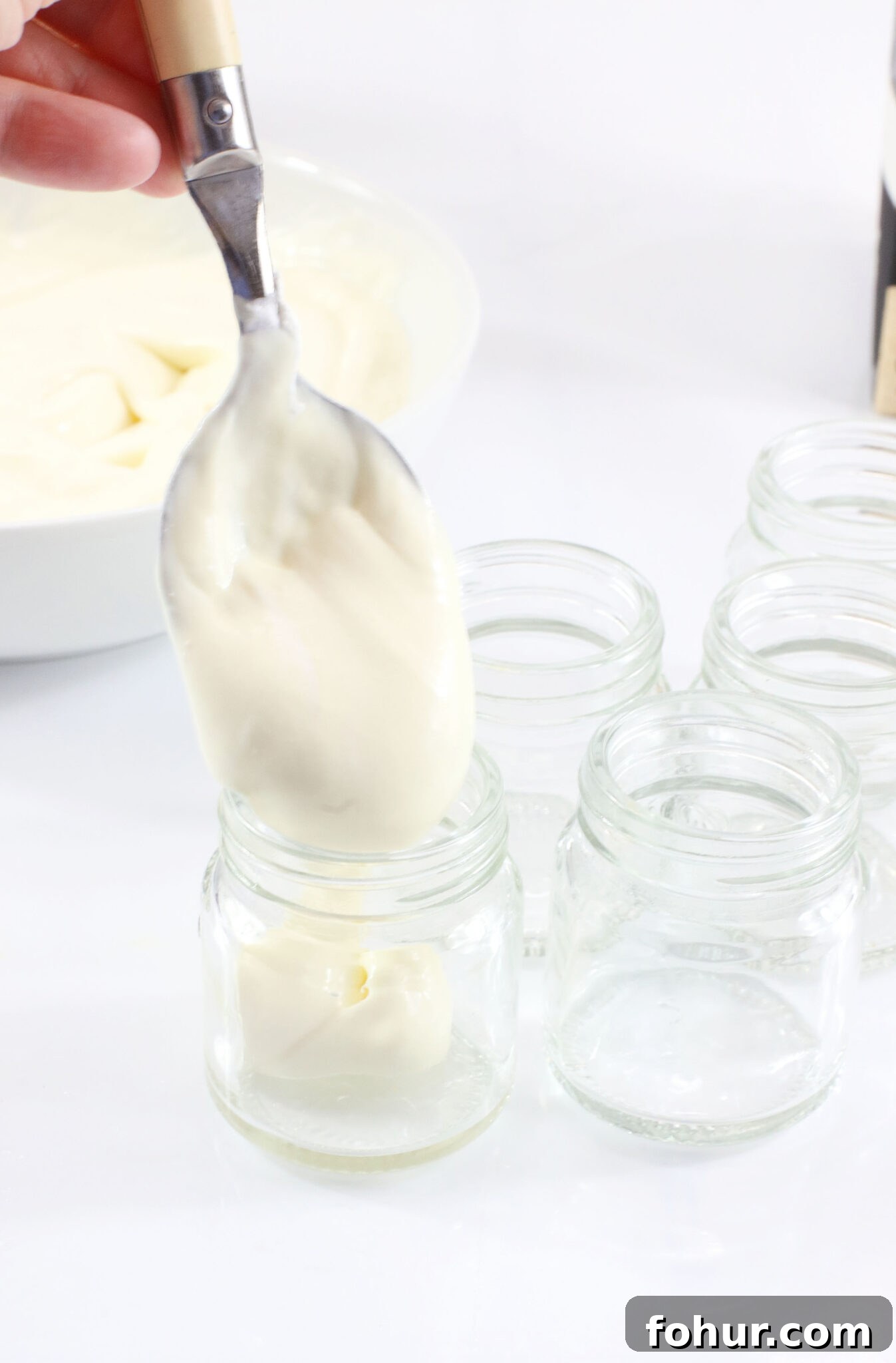 Creamy Eggnog Pudding Shots for Holiday Parties 5 hand using spoon to fill mini mason jars with boozy pudding mixture