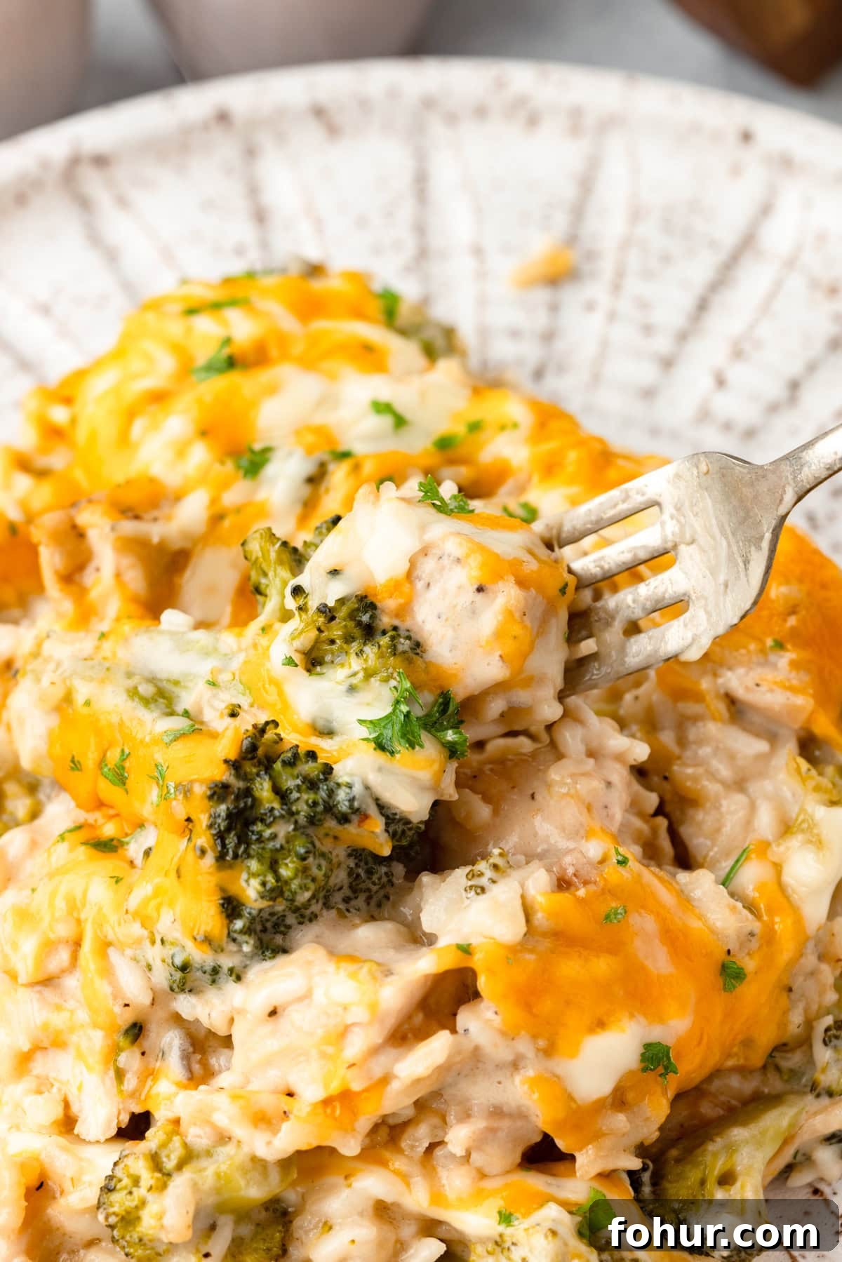 Creamy Cheesy Chicken Broccoli and Rice Casserole 7 A close-up of a forkful of Cheesy Chicken Broccoli and Rice Casserole on a plate, featuring melted cheese, broccoli florets, tender chicken pieces, and creamy rice.