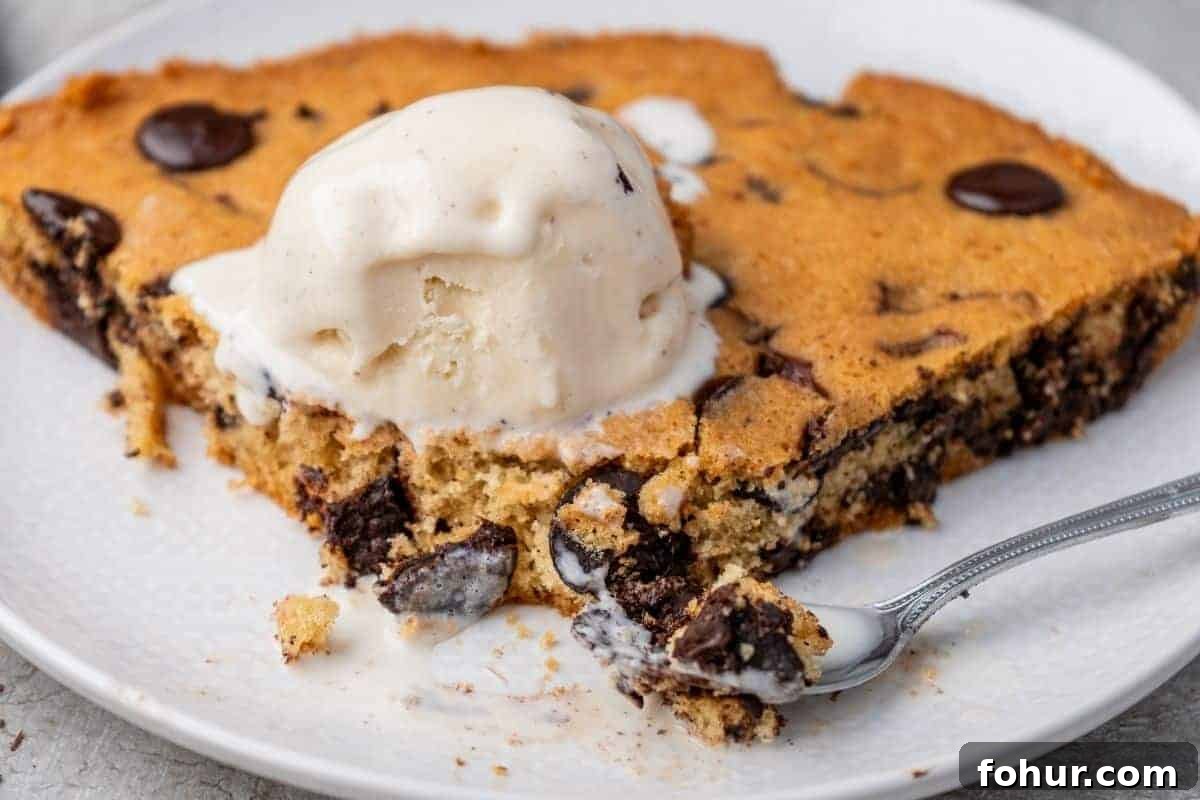 19 Cookie Recipes Even Dessert Skeptics Can't Resist 15 A slice of chocolate chip skillet cookie topped with a scoop of vanilla ice cream sits on a white plate with a spoon.