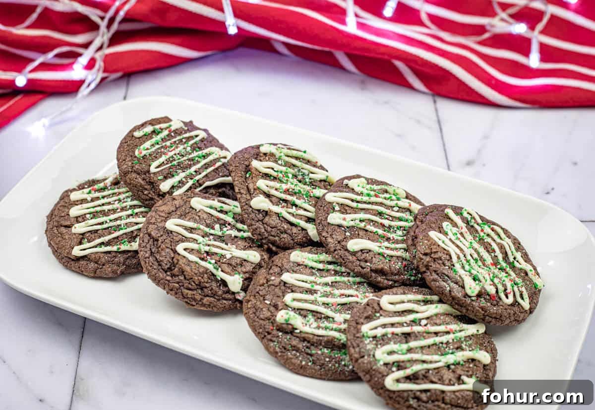 19 Cookie Recipes Even Dessert Skeptics Can't Resist 17 A plate of chocolate cookies topped with white icing and green sprinkles. A red and white striped cloth is in the background.
