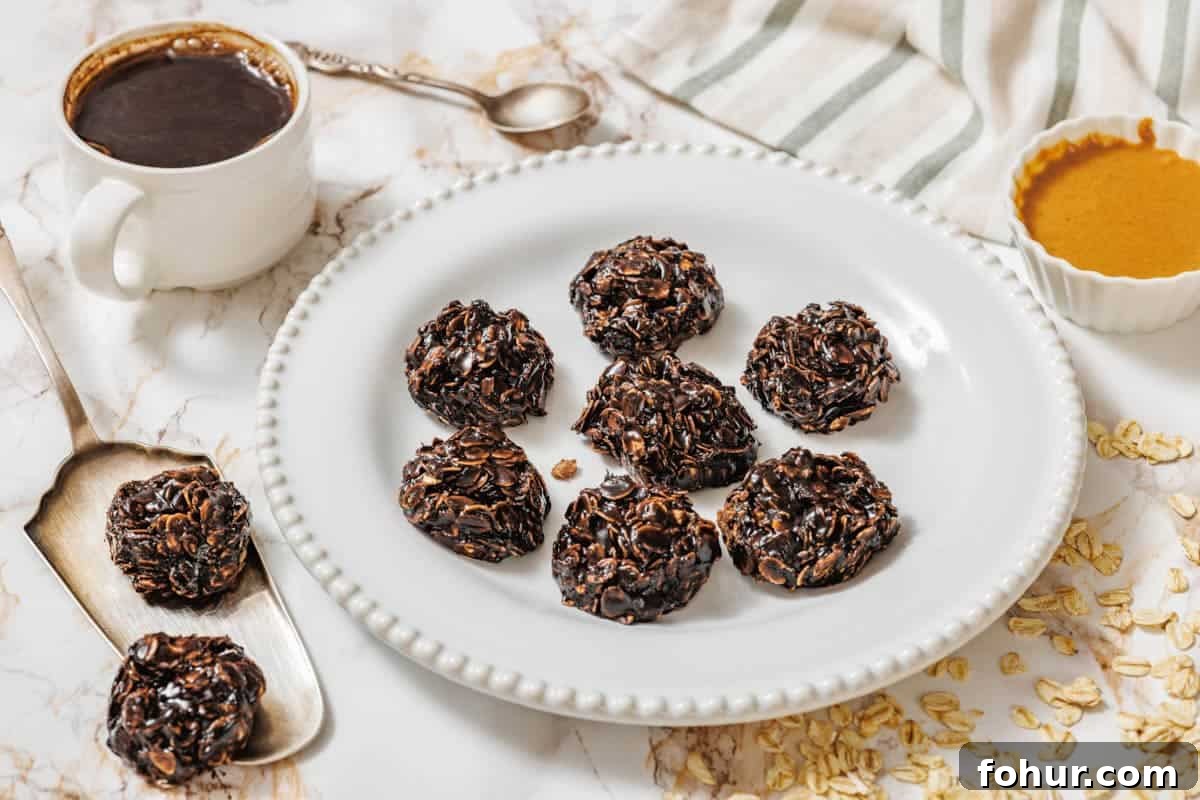 19 Cookie Recipes Even Dessert Skeptics Can't Resist 9 A white plate with seven Peanut Butter No-Bake Cookies on a marble surface, surrounded by a cup of coffee, a spoon, a bowl of nut butter, oats, and a striped cloth.