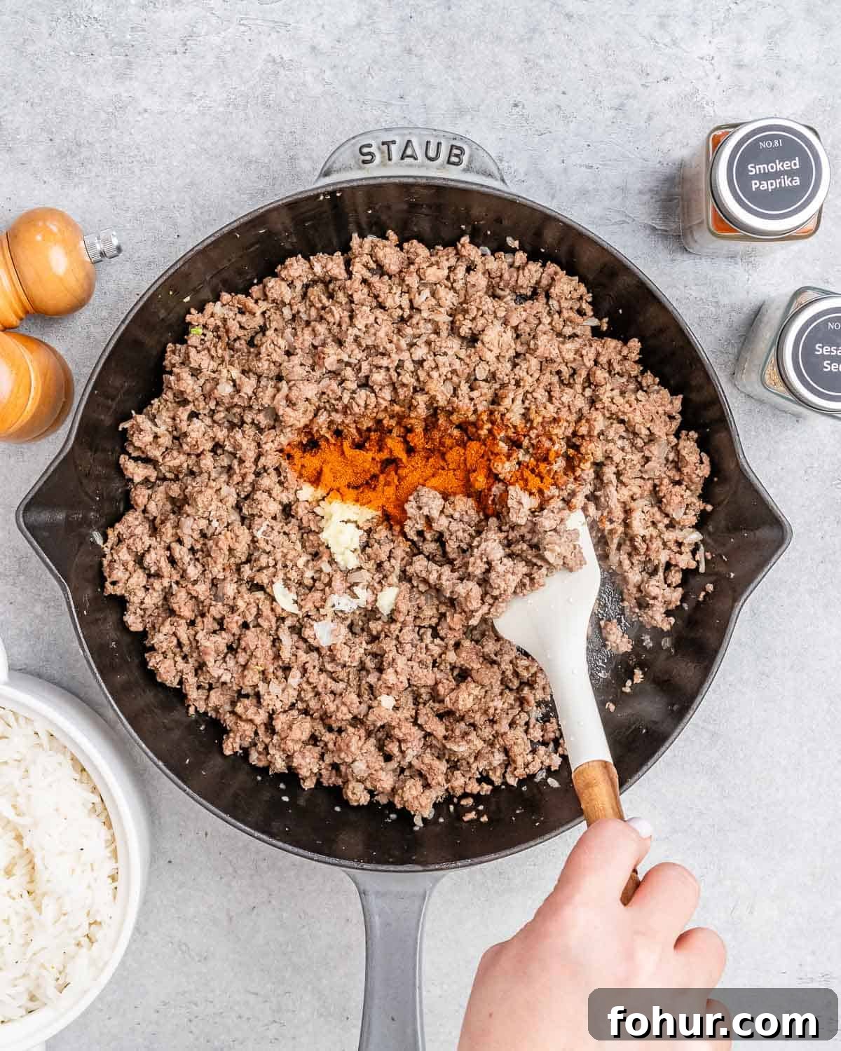 Stirring in spices to ground beef in a skillet.