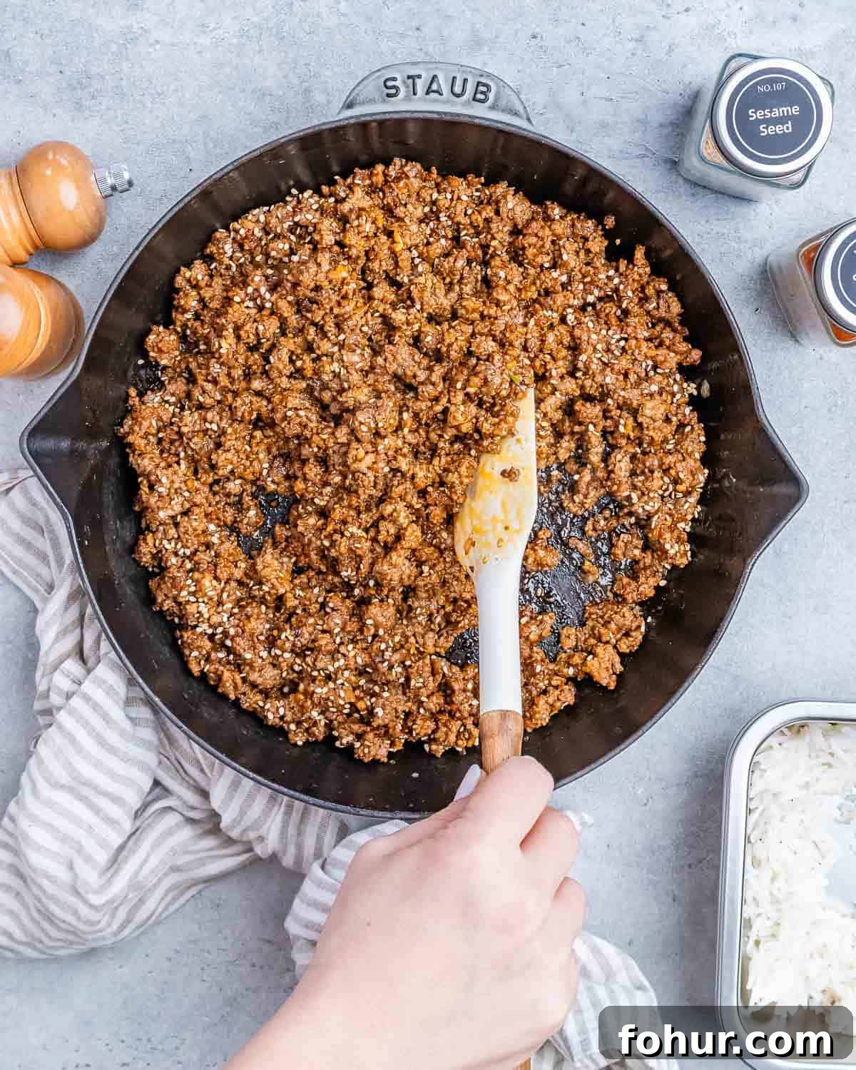 Stirring ground beef in a skillet with a white spatula.