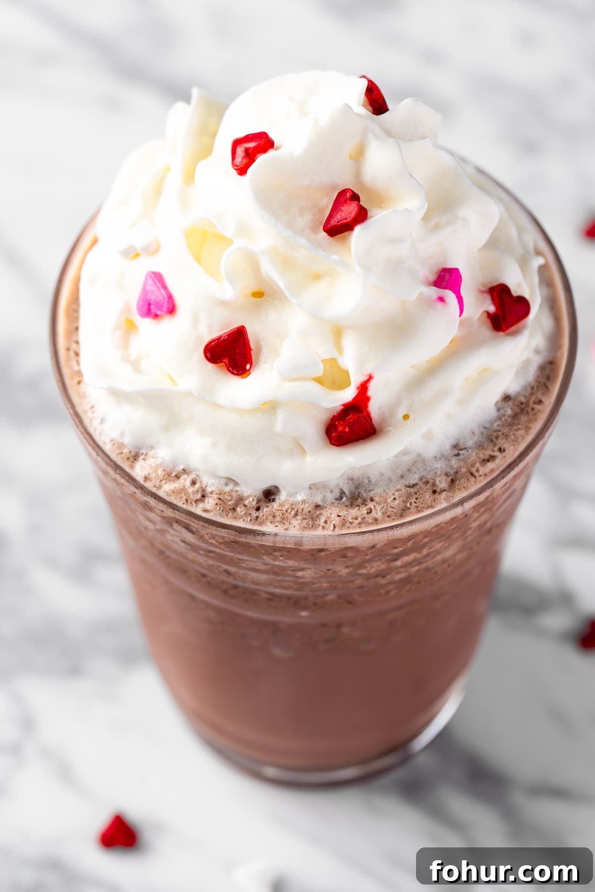 A red velvet frappuccino topped with whipped cream and heart sprinkles.