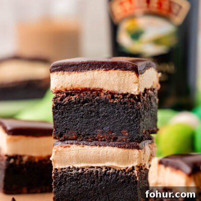 Decadent Baileys Irish Cream Brownies Recipe 9 Two brownies with irish cream frosting and ganache topping stacked on a piece of parchment paper.