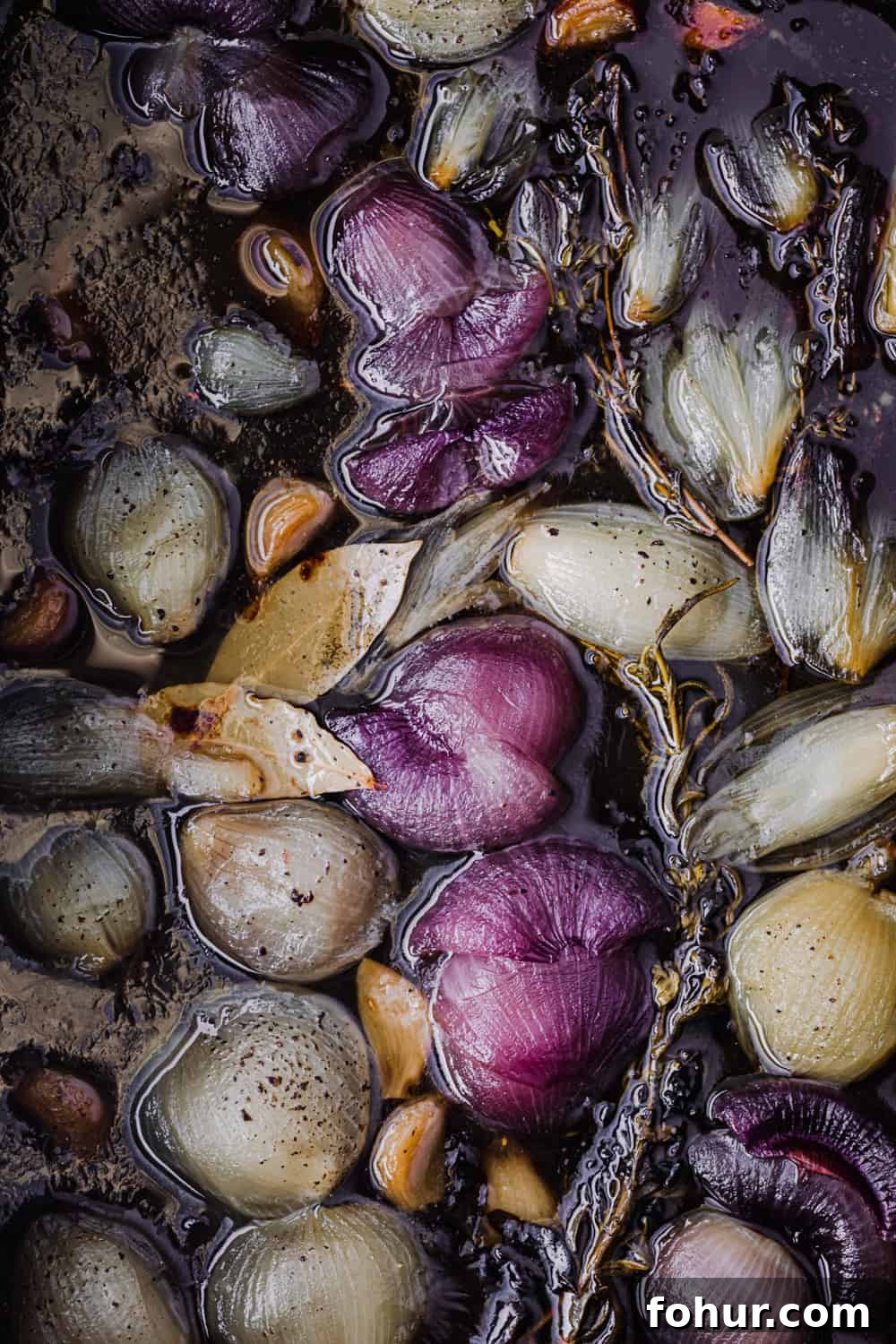 Shallot Confit Recipe: Jammy Slow-Roasted Condiment for Any Dish 2 Shallot confit just out of the oven, with roasted shallots and garlic submerged in olive oil and fresh herbs.