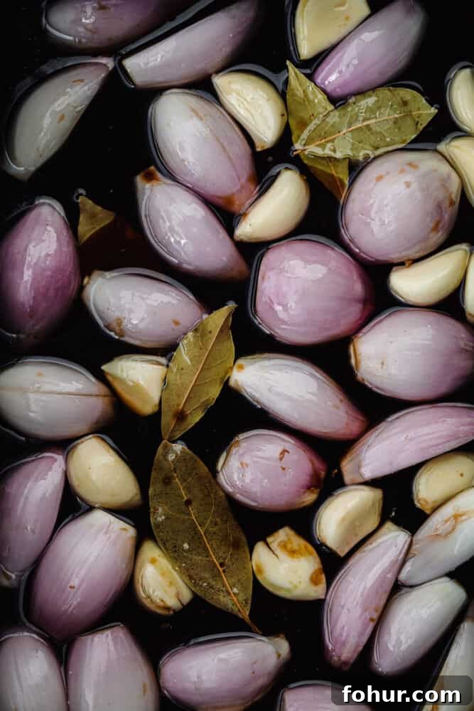 Shallot Confit Recipe: Jammy Slow-Roasted Condiment for Any Dish 6 Whole shallots and garlic submerged in olive oil with bay leaves before roasting for shallot confit.