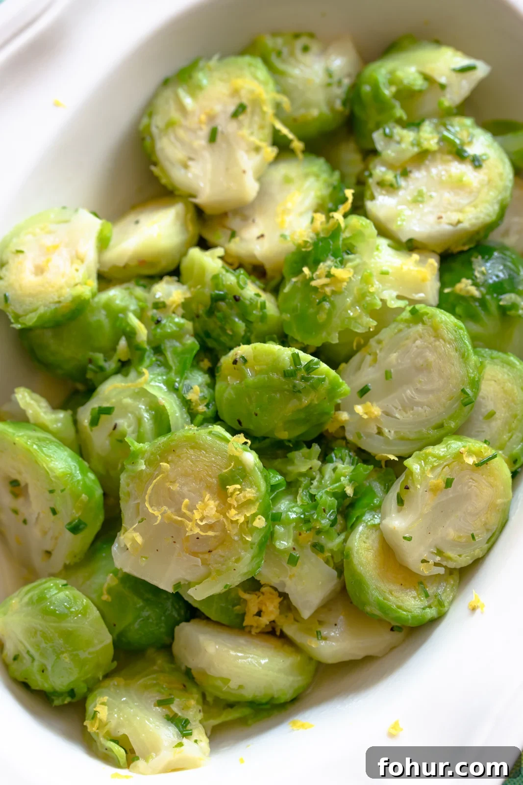 Crispy Lemon Roasted Brussels Sprouts 2 Brussels sprouts with lemon in a white scalloped serving dish